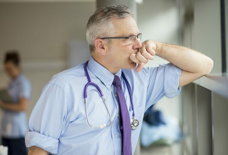 5thPort eConsent Software – Healthcare Doctor Burnout – Panel 3 5thPort patient engagement and eConsent software - An exhausted doctor looks out of the window in a hospital. With 5thPort's digital eConsent software, this kind of clinician burnout can be greatly reduced.